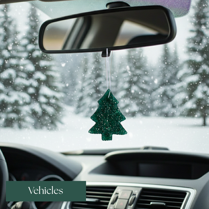 Green Christmas tree ornament hanging from a car's rearview mirror with a snowy outdoor background.