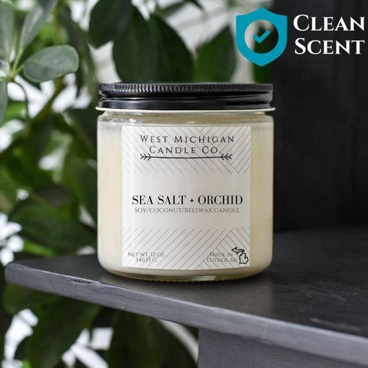 West Michigan Candle Co. candle labeled 'Sea Salt + Orchid' on a dark surface with greenery in the background.